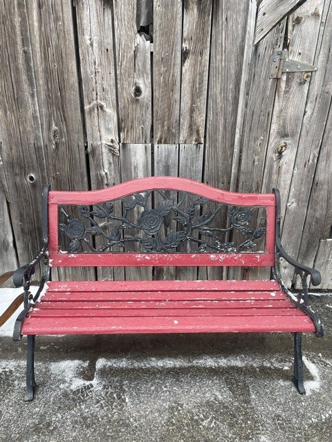 Red wooden bench with decorative metal back against a wooden wall.