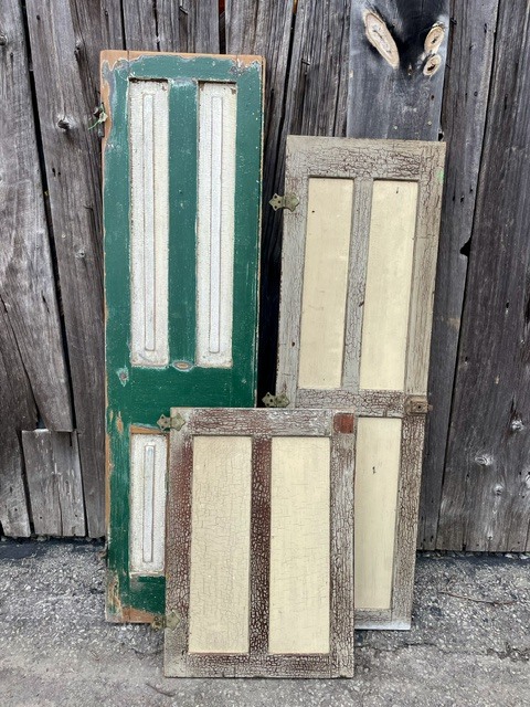 Old wooden cabinet doors leaning against a weathered wooden wall.