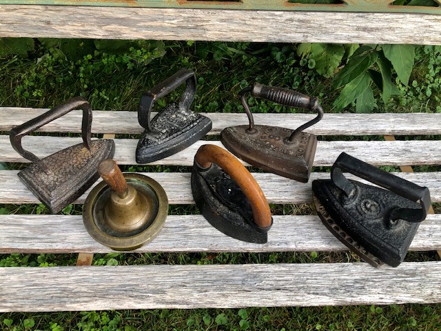 5 antique flat irons on top of a wooden bench