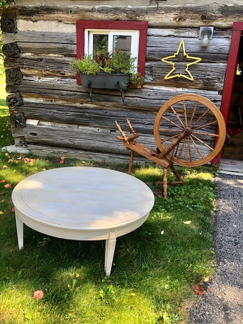 white round table with wooden cabin and wooden wheel in the background