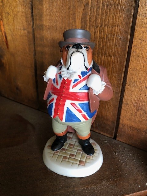 standing dog figurine wearing a hat, a coat, and United Kingdom's flag underneath
