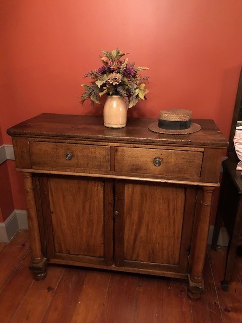 two door two drawers top cabinet with flower in a vase and hat on top