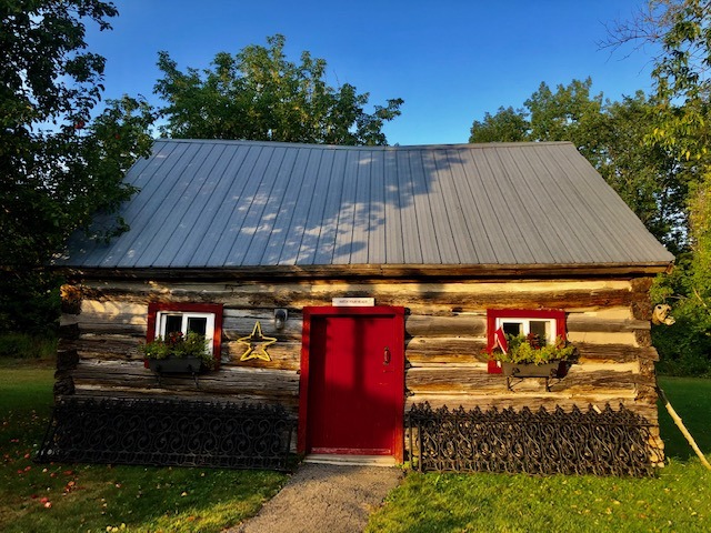 wooden cabin with trees in the background and fence at front.