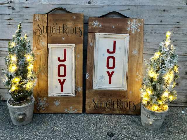 two wooden signs advertising sleigh rides between two ornamental christmas trees in pots