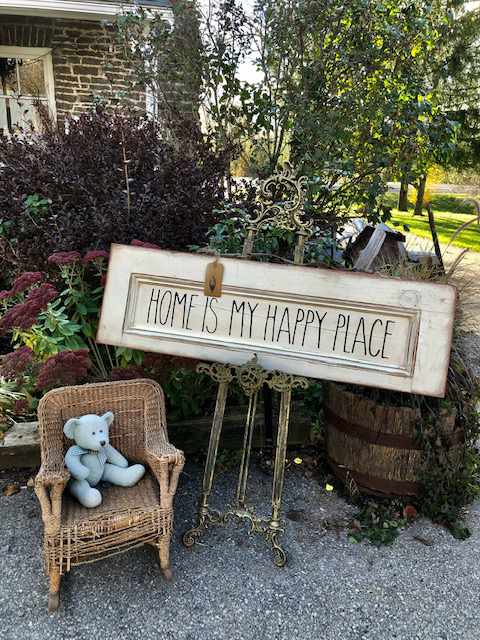a knitted bear on a wicker chair in front of a sign saying "home is my happy place"