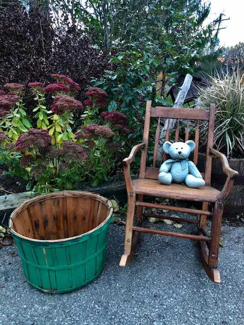 knitted teddy bear on a wooden rocking chair next to a wooden basket