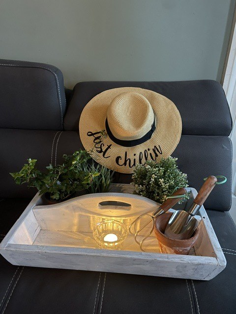 Tray with gardening tools, plants, and a straw hat on a leather couch.