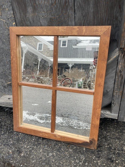 Wood-framed window pane reflecting an outdoor rustic scene.