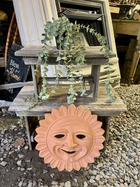 Wooden plant stand with trailing greenery and a sun face decoration below.