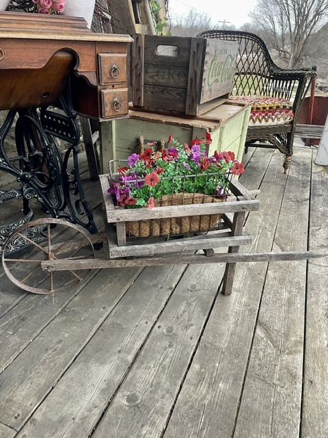 Wooden plant cart with colorful flowers on a porch among vintage furniture.
