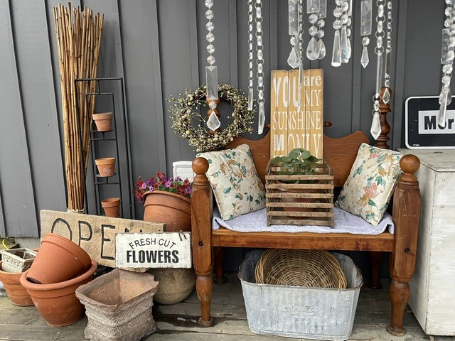 Rustic bench display with pillows, hanging crystals, and garden decor items.